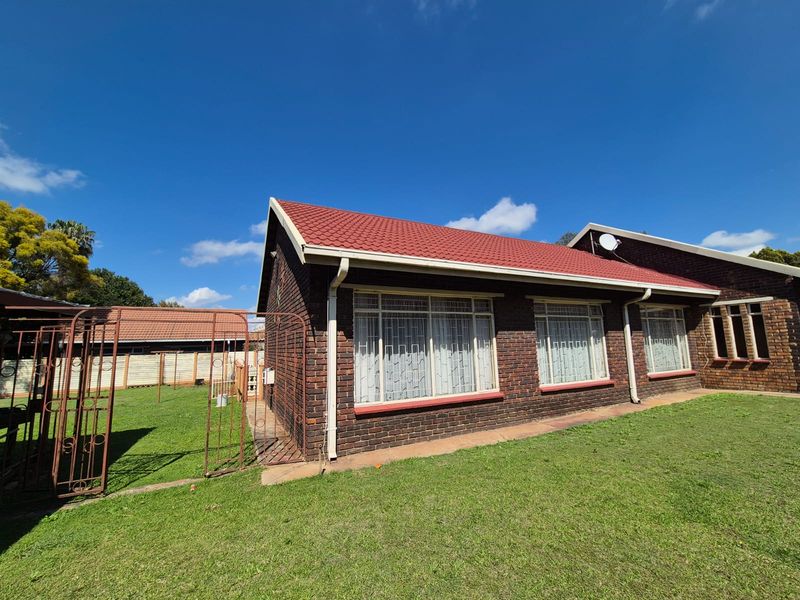 Rear view of a face brick house featuring a tiled roof, large windows with security bars, and a surrounding lawn area.