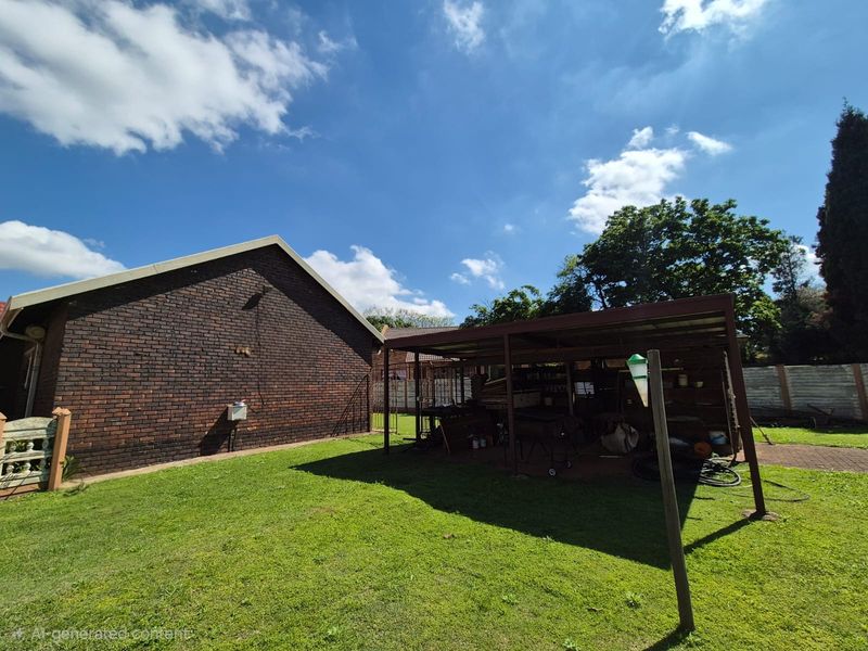 Rear garden area featuring a brick exterior wall, a metal carport structure, and a paved walkway leading through the lawn.