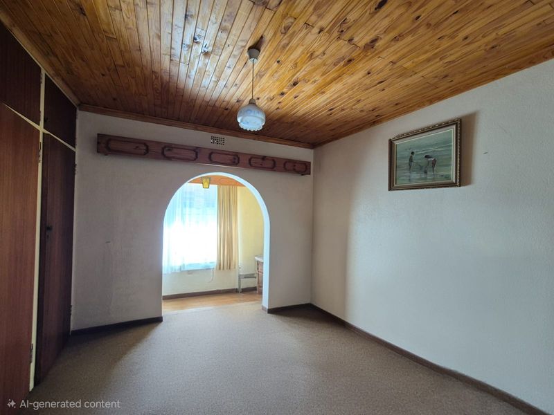 An empty living room featuring a timber tongue and groove ceiling, an arched doorway leading to an adjacent space, and built-in storage cupboards.