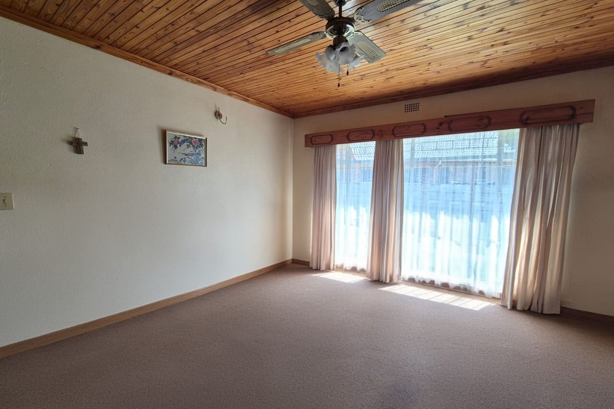 Spacious living room featuring a warm timber tongue and groove ceiling, ceiling fan, and large windows allowing for ample natural light.