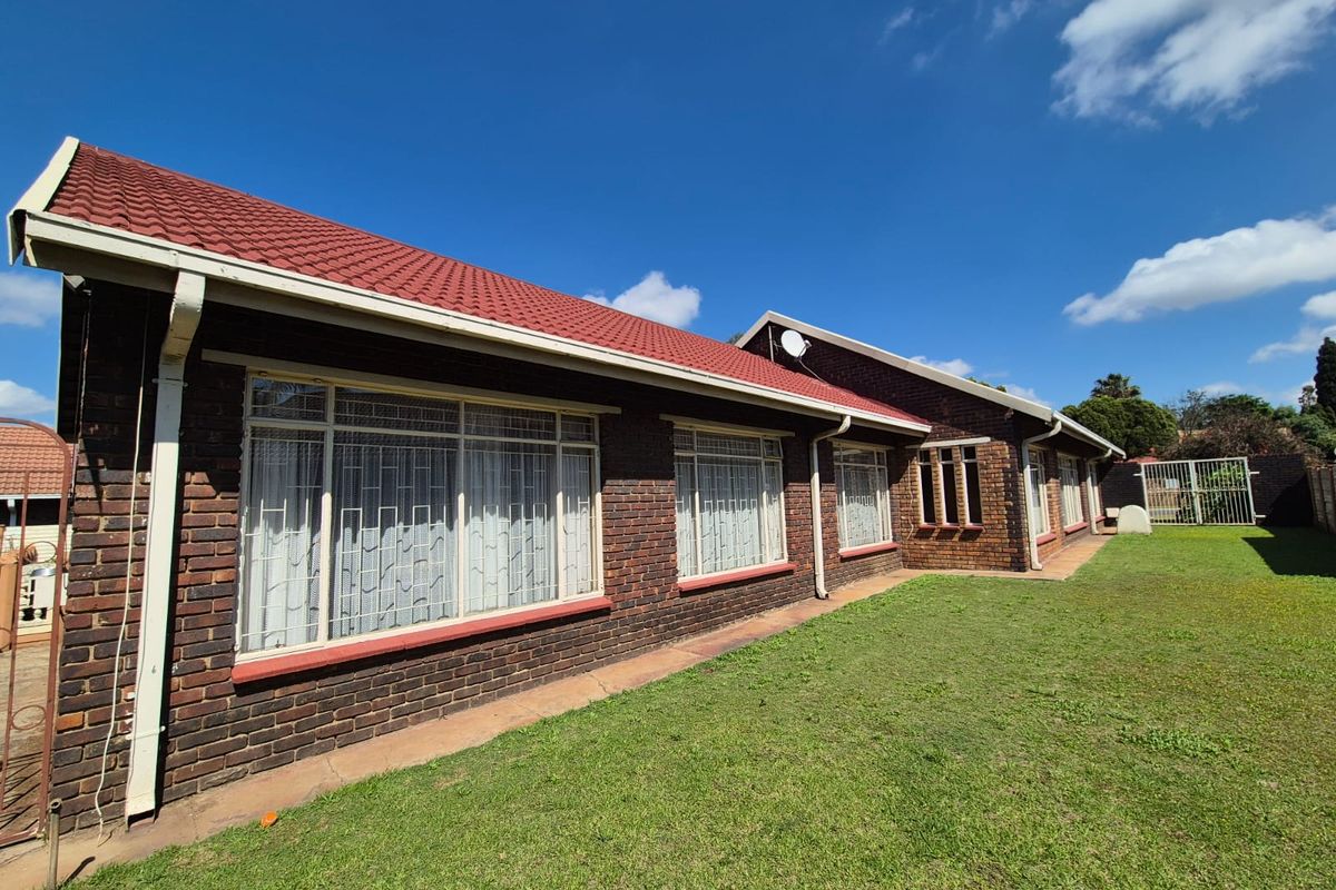 Rear view of a face brick house featuring a tiled roof, security bars on windows, and a well-maintained lawn.