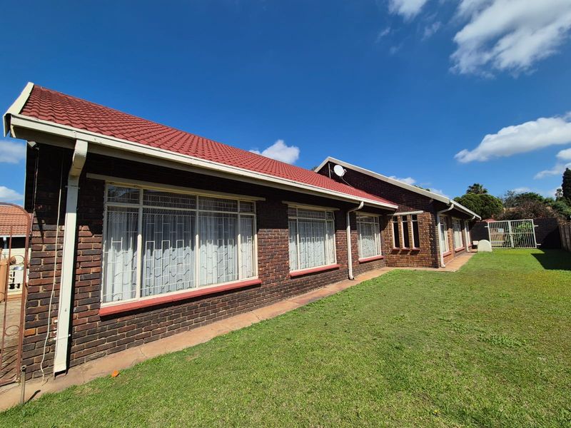 Rear view of a face brick house featuring a tiled roof, security bars on windows, and a well-maintained lawn.