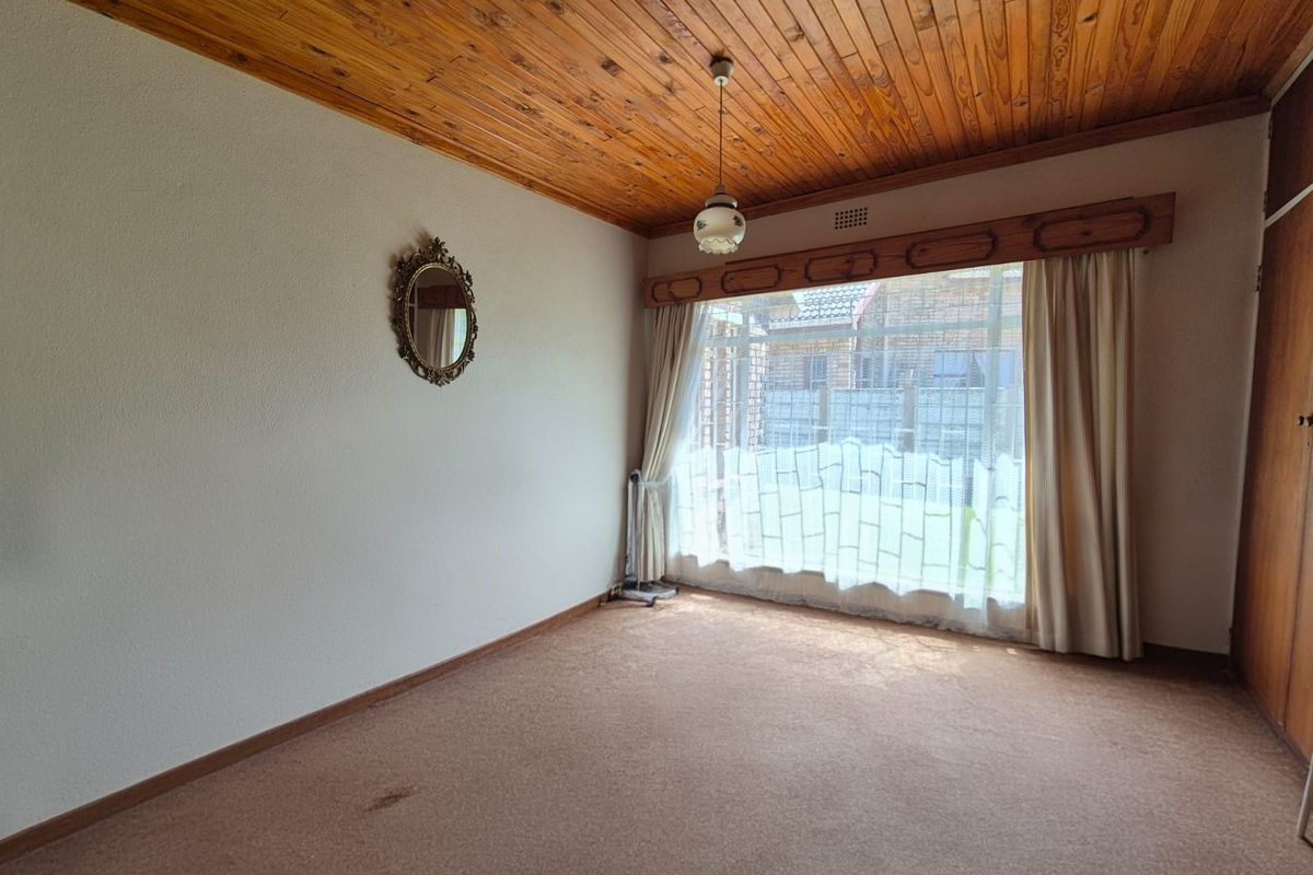 A spacious bedroom featuring a distinctive timber tongue and groove ceiling, built-in wardrobe, and large window allowing for natural light.