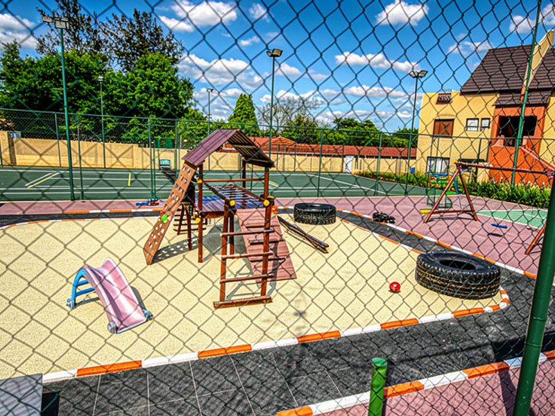A communal outdoor recreational area featuring a fenced tennis court and a dedicated children's playground with sand pit and climbing equipment.