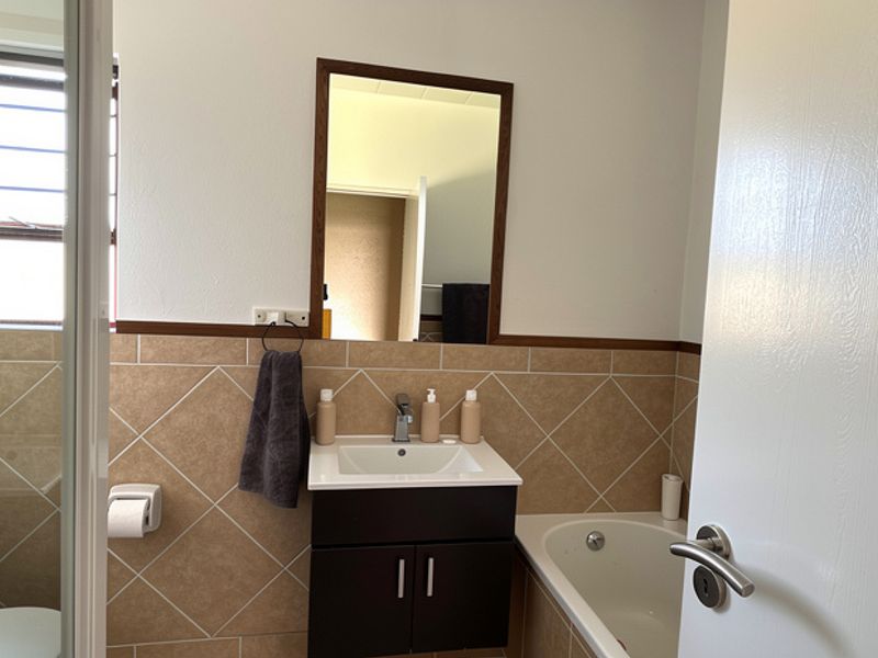 A functional bathroom featuring a vanity cabinet with basin, a bathtub, a separate shower enclosure, and neutral wall tiling.
