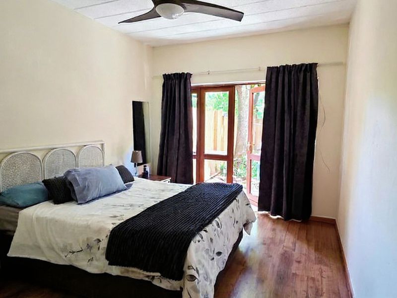 A bedroom featuring laminate flooring, a ceiling fan, and a glass panel door providing access to the exterior.