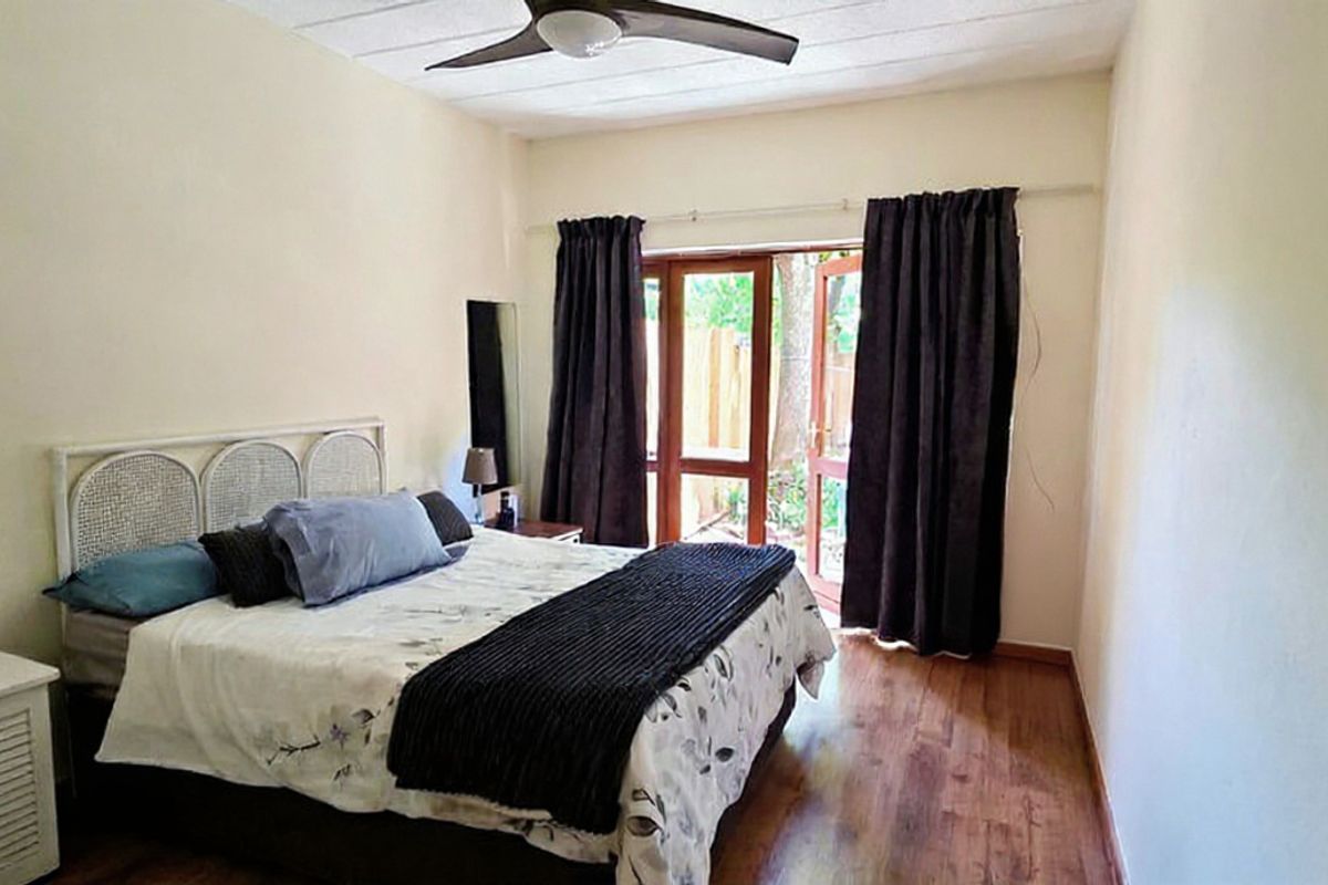A bedroom featuring laminate flooring, a ceiling fan, and a glass panel door providing access to the exterior.