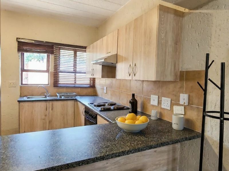 Functional kitchen featuring light wood-finish cabinetry, granite countertops, a built-in electric hob with extractor fan, and a tiled backsplash.