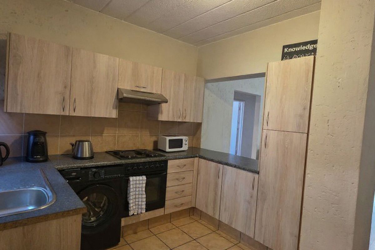 Functional kitchen featuring light wood-look cabinetry, stone-effect countertops, built-in oven with gas hob, and tiled flooring with a convenient serving hatch.