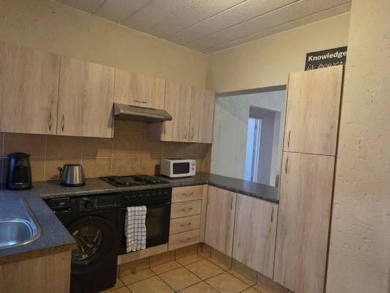 Functional kitchen featuring light wood-look cabinetry, stone-effect countertops, built-in oven with gas hob, and tiled flooring with a convenient serving hatch.