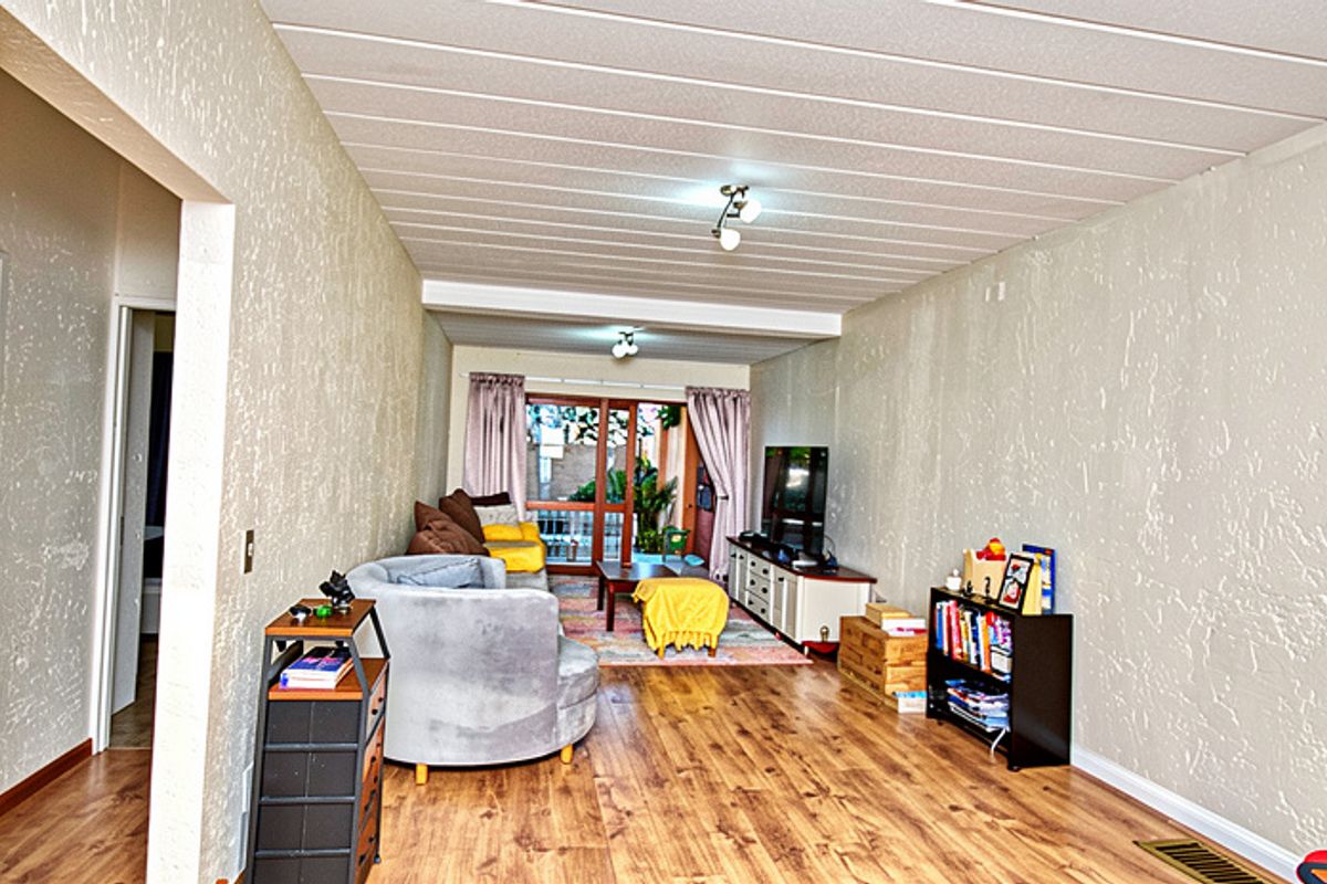 A living room featuring laminate flooring, textured walls, and a slatted ceiling, with a sliding glass door providing access to the outdoor area.