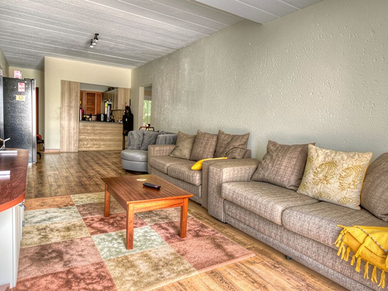 Open plan living area featuring laminate flooring, textured walls, and an exposed beam ceiling, flowing into a functional kitchen space.