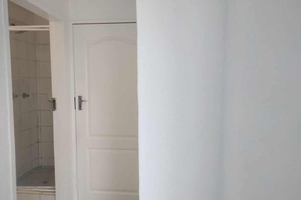 A functional bathroom featuring a tiled shower enclosure and a standard internal door, presenting a clean but dated aesthetic.