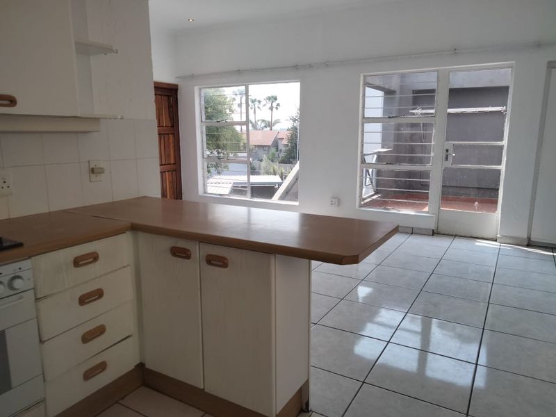 An open-plan kitchen and living area featuring tiled flooring, built-in cabinetry, and direct access to an outdoor balcony through glass doors.
