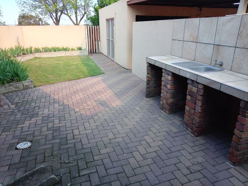 Outdoor patio area featuring a built-in brick braai with a tiled countertop and sink, adjacent to a small lawn and paved courtyard.