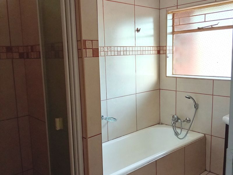 A functional bathroom featuring a built-in bathtub, separate shower enclosure, and neutral wall and floor tiling with an obscured glass window.