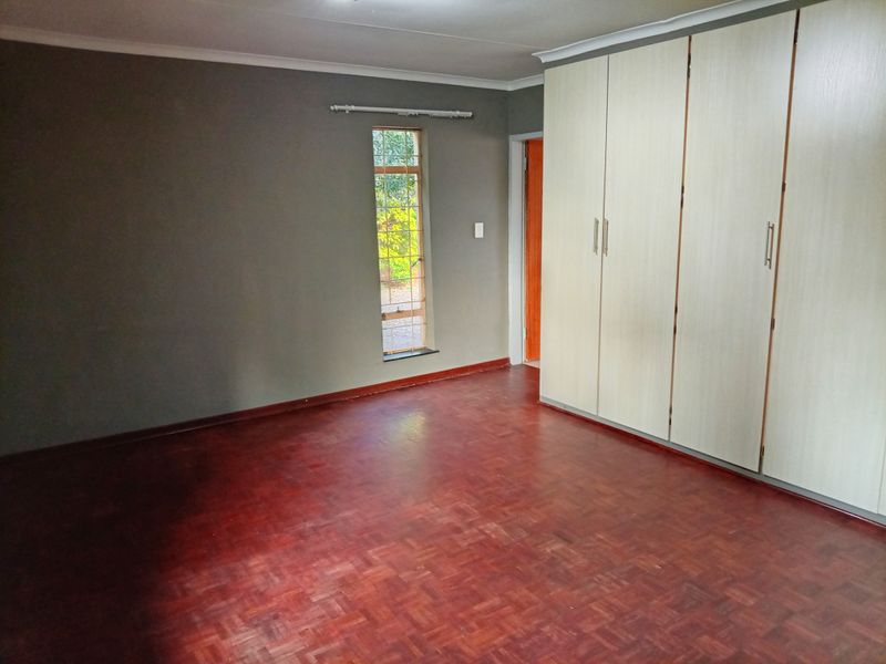 A spacious bedroom featuring classic parquet flooring and extensive built-in cupboard storage, offering a neutral canvas ready for personalization.
