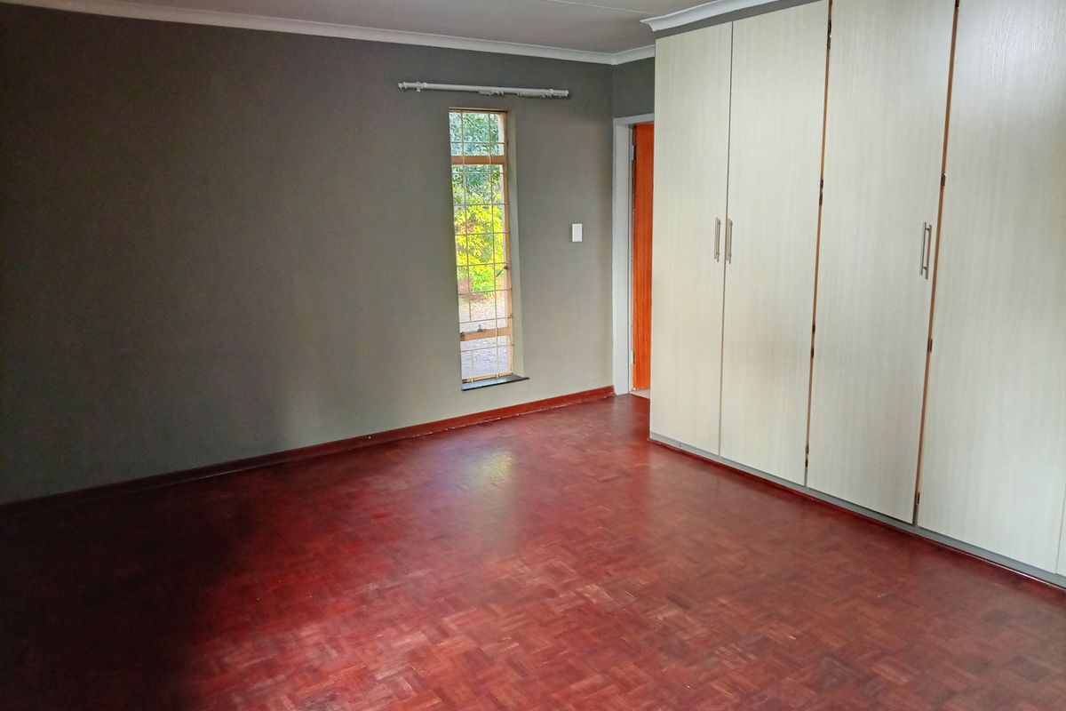 A spacious bedroom featuring classic parquet flooring and extensive built-in cupboard storage, offering a neutral canvas ready for personalization.