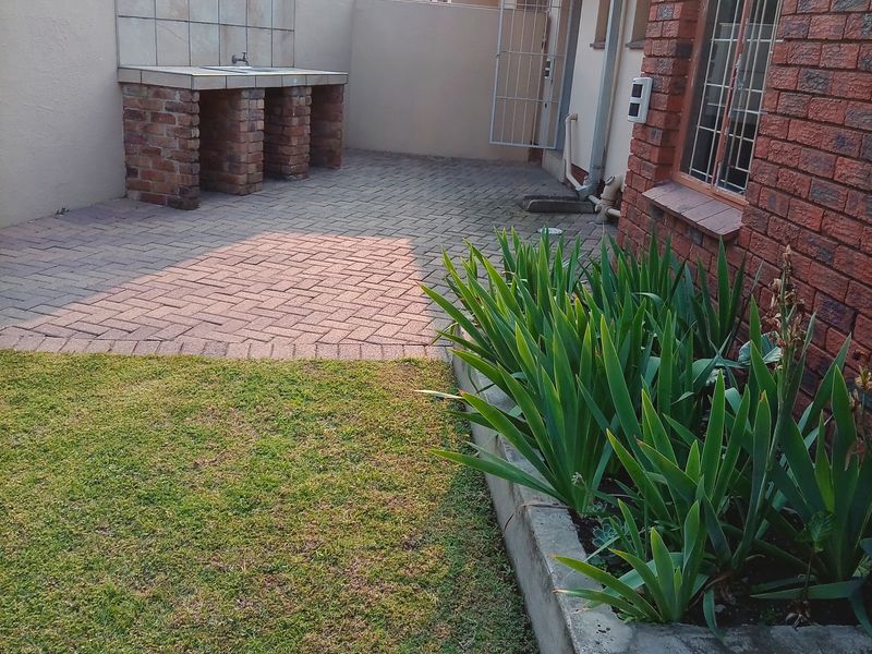 A paved outdoor patio area featuring a built-in brick braai, concrete planter, and direct access to the home via a security gate.