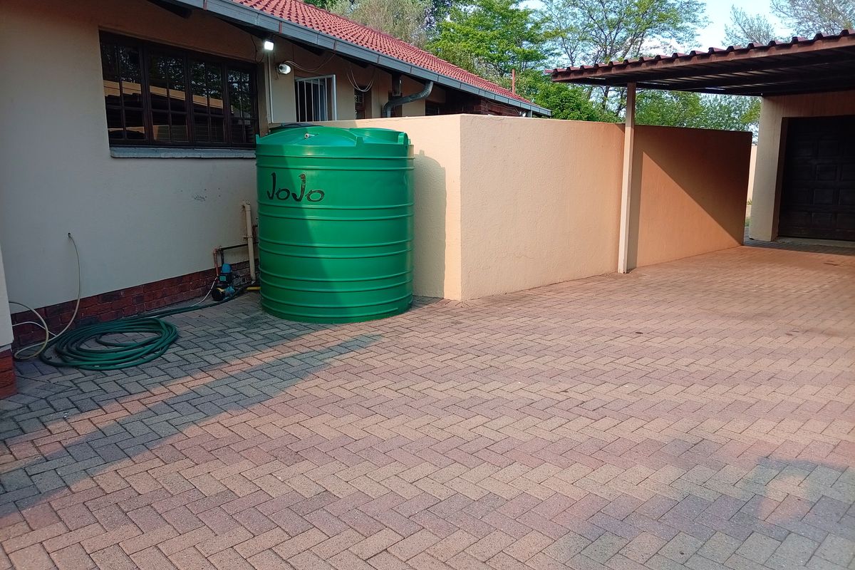 Rear exterior area featuring a paved driveway, carport, and a Jojo water storage tank with an integrated pump system.