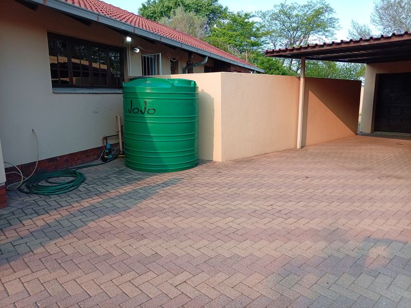 Rear exterior area featuring a paved driveway, carport, and a Jojo water storage tank with an integrated pump system.