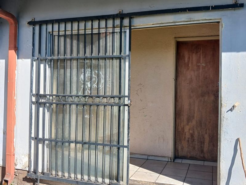 Exterior view of a rear entrance featuring a sliding security gate, tiled threshold, and weathered wall finishes requiring maintenance.