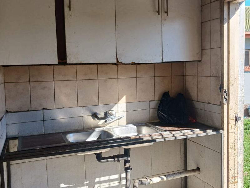 A functional scullery or utility area featuring a double sink, tiled splashback, and overhead cabinetry, requiring cosmetic updates and maintenance.