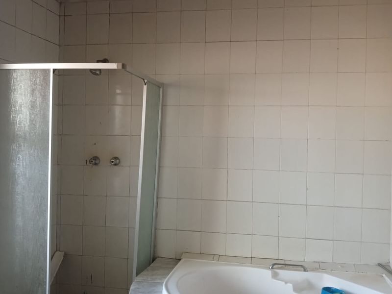 A dated bathroom featuring a built-in corner bathtub and a separate shower enclosure, requiring significant renovation and cosmetic updates to the ceiling and tiling.