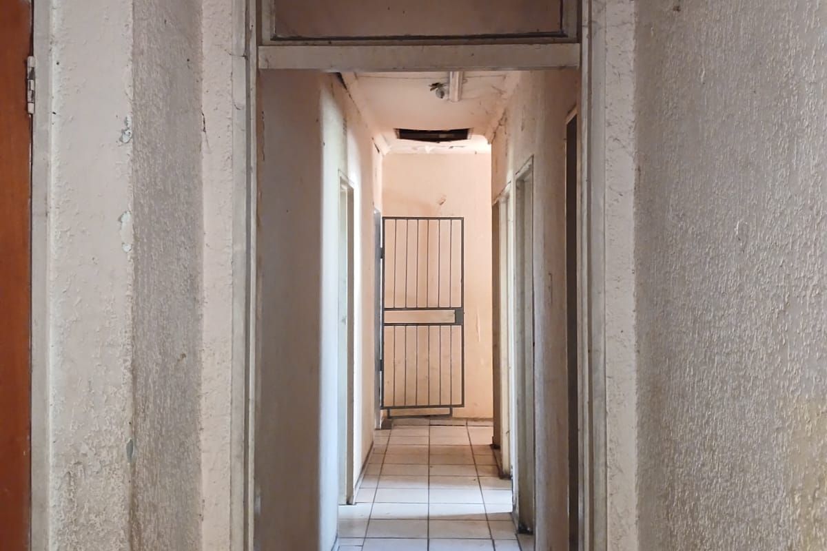 A narrow interior hallway featuring tiled flooring and a security gate, showing significant signs of wear and requiring cosmetic refurbishment.