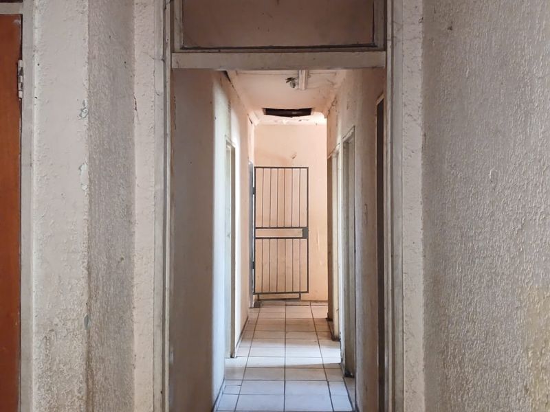 A narrow interior hallway featuring tiled flooring and a security gate, showing significant signs of wear and requiring cosmetic refurbishment.