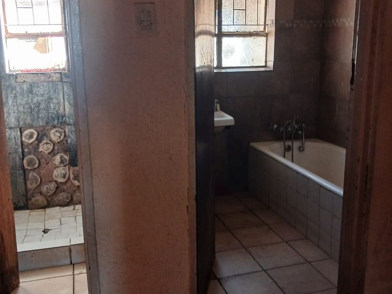 A dated bathroom featuring a bathtub, wall-mounted basin, and tiled finishes, requiring significant renovation and cosmetic updates to improve its condition.