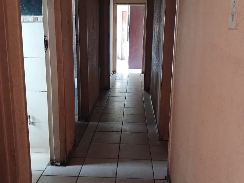 A narrow interior hallway featuring tiled flooring and multiple doorways, showing signs of wear and ceiling water damage requiring maintenance.