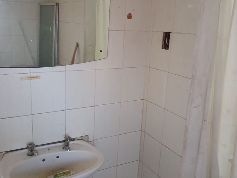 A dated bathroom featuring a pedestal basin and tiled walls, currently requiring renovation and repair to the wall finishes and electrical fixtures.