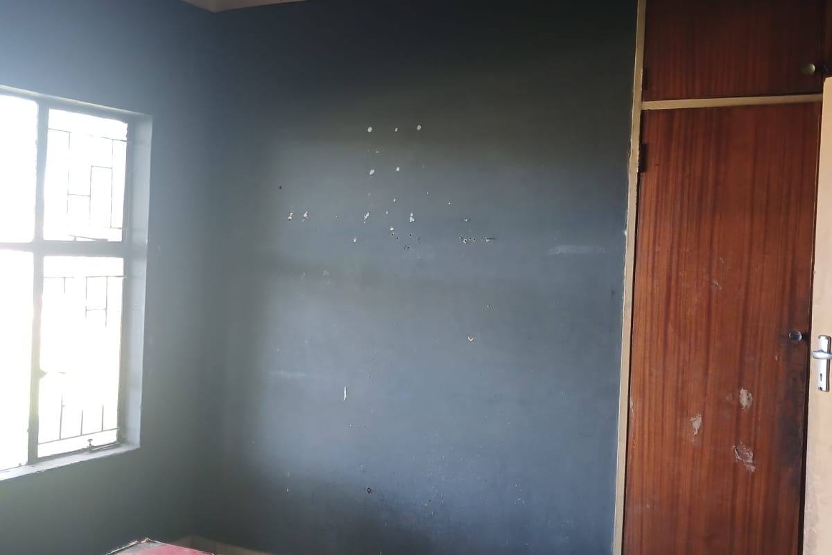 An empty bedroom featuring tiled flooring, a built-in cupboard, and security bars on the window. The room requires cosmetic updates to the walls and ceiling.