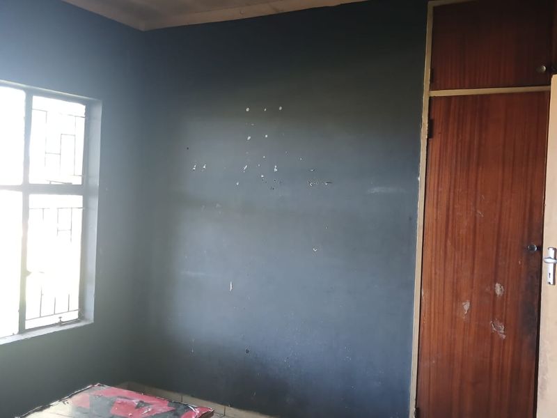 An empty bedroom featuring tiled flooring, a built-in cupboard, and security bars on the window. The room requires cosmetic updates to the walls and ceiling.