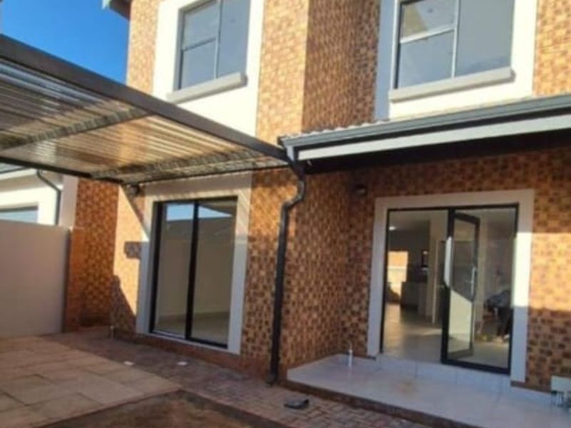 Rear view of a modern townhouse featuring a brick facade, covered patio area, and paved courtyard with an unfinished garden section.