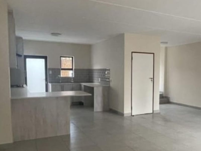 Spacious open-plan living area featuring neutral tiled flooring and a functional kitchen with built-in cabinetry and countertops.