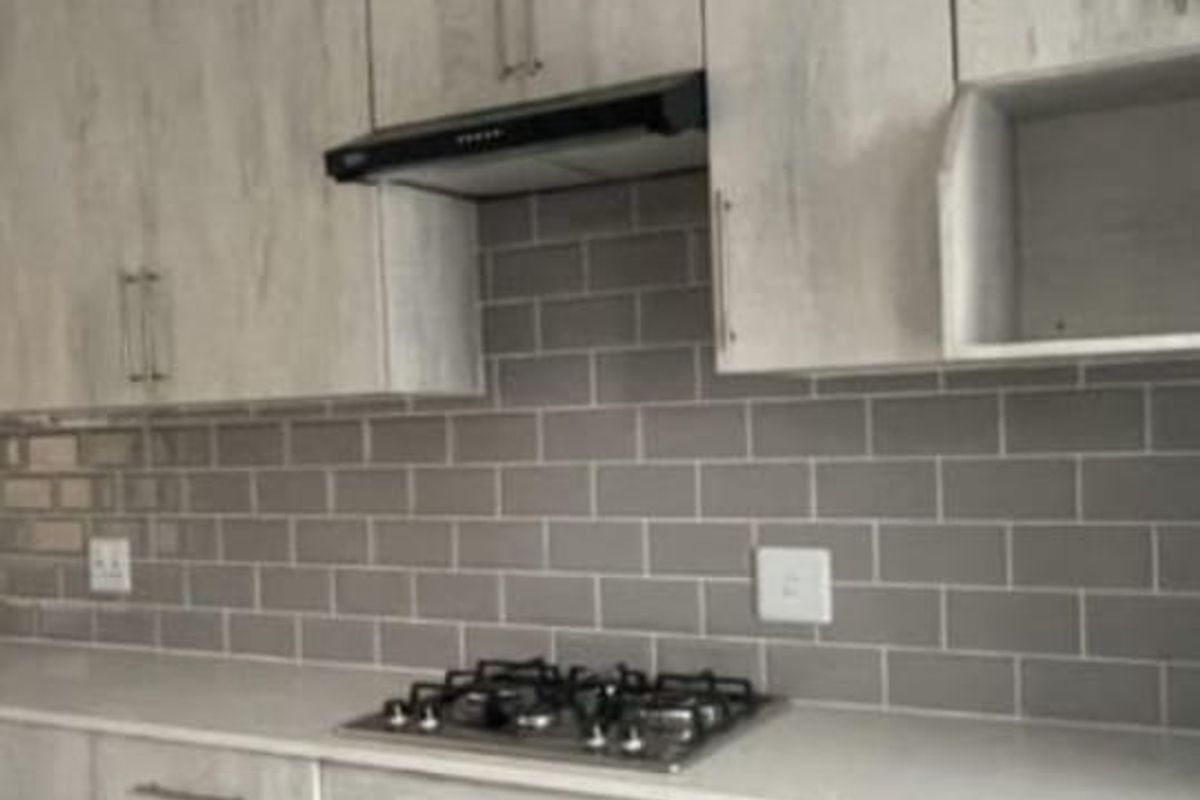 Modern kitchen featuring light wood-grain cabinetry, subway tile backsplash, stone countertops, and integrated stainless steel gas hob and oven.
