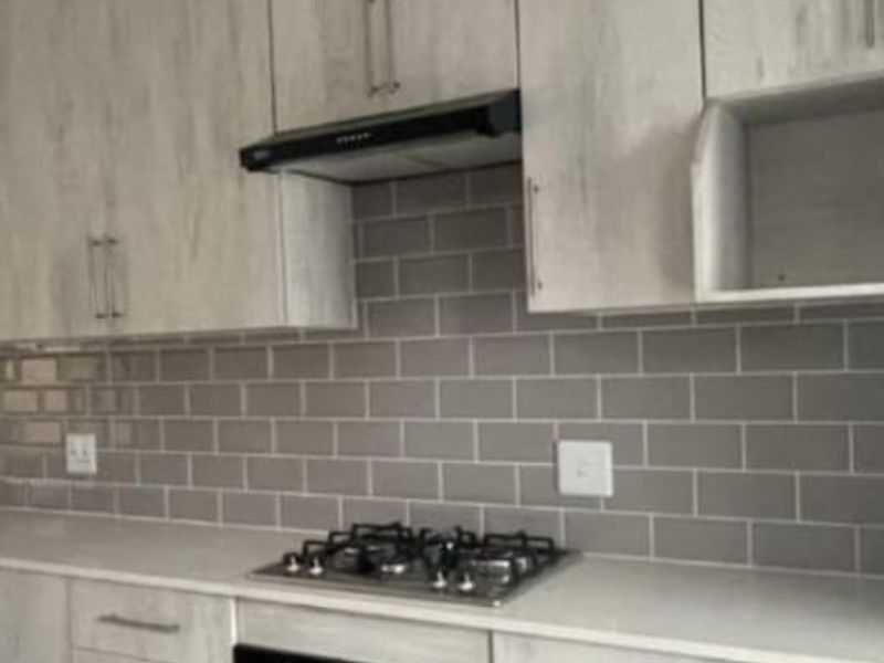 Modern kitchen featuring light wood-grain cabinetry, subway tile backsplash, stone countertops, and integrated stainless steel gas hob and oven.