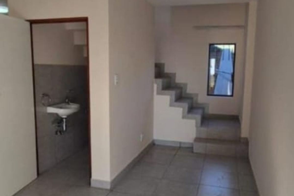 An empty hallway featuring tiled flooring, a staircase leading to the upper level, and a small adjacent washroom area.
