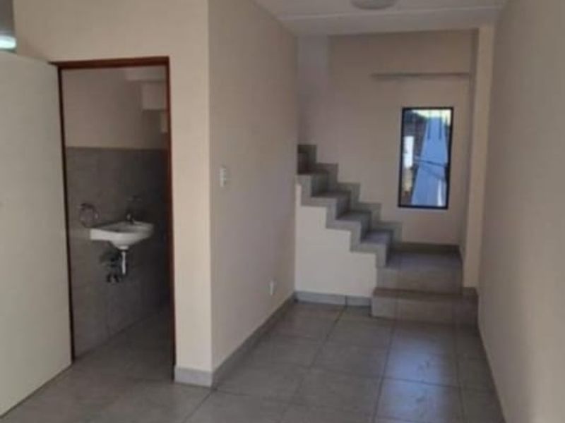 An empty hallway featuring tiled flooring, a staircase leading to the upper level, and a small adjacent washroom area.
