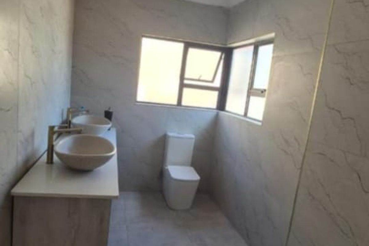 Modern bathroom featuring a double vanity with vessel sinks, a walk-in shower with tiled flooring, and neutral wall tiling throughout.