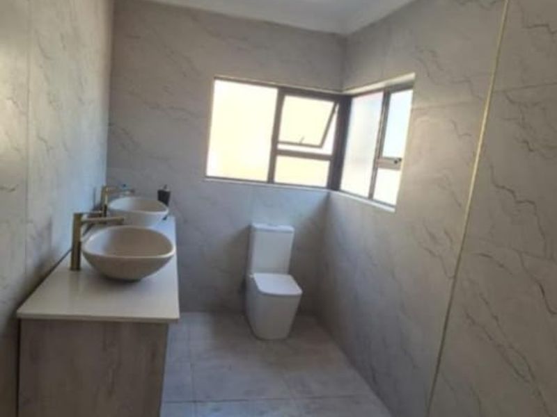 Modern bathroom featuring a double vanity with vessel sinks, a walk-in shower with tiled flooring, and neutral wall tiling throughout.