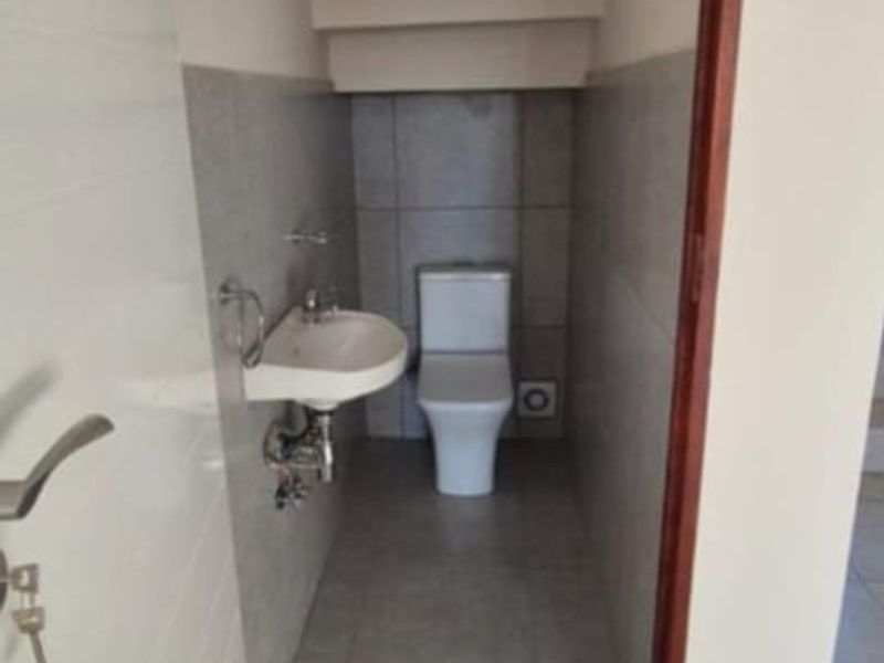 A compact guest bathroom located under the staircase, featuring a modern toilet and wall-mounted basin with neutral floor and wall tiling.