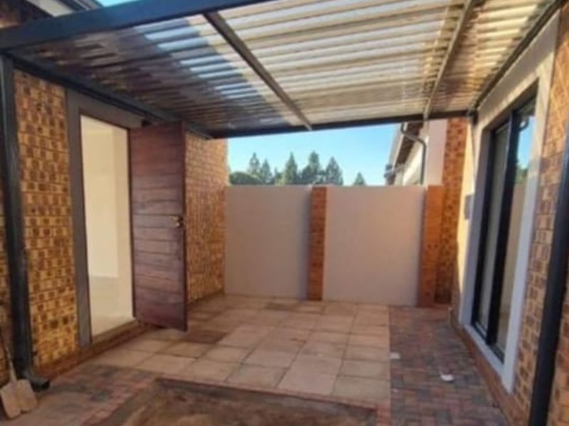 A covered outdoor patio area featuring a corrugated roof, paved flooring, and direct access to the interior through a sliding glass door.