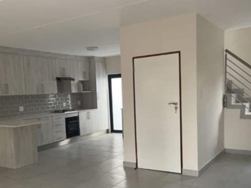 Open-plan living area featuring a modern kitchen with built-in cabinetry, oven, hob, and extractor fan, complemented by tiled flooring and an adjacent staircase.