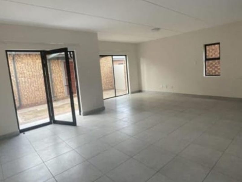 A spacious, empty living area featuring neutral tiled flooring and large sliding glass doors that provide access to the outdoor space.