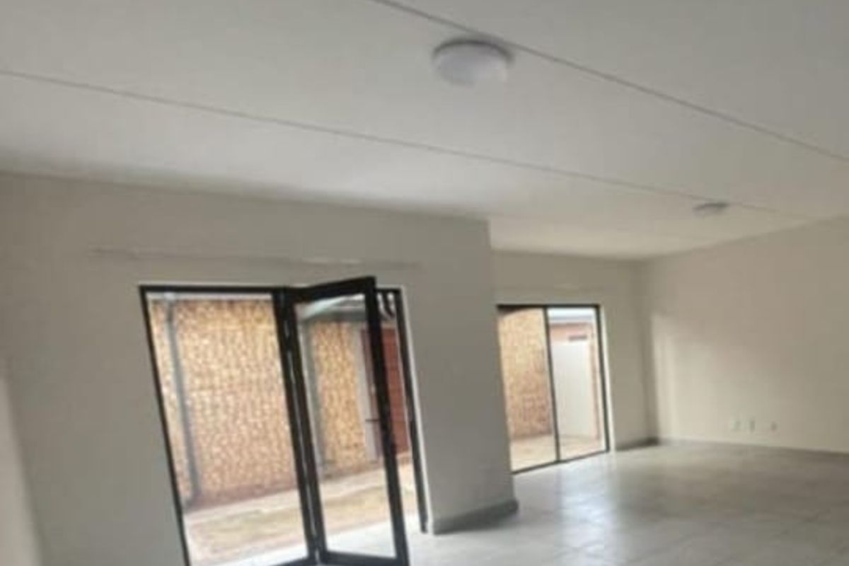 Spacious, empty living area featuring neutral tiled flooring and large aluminium framed glass doors providing access to the exterior.