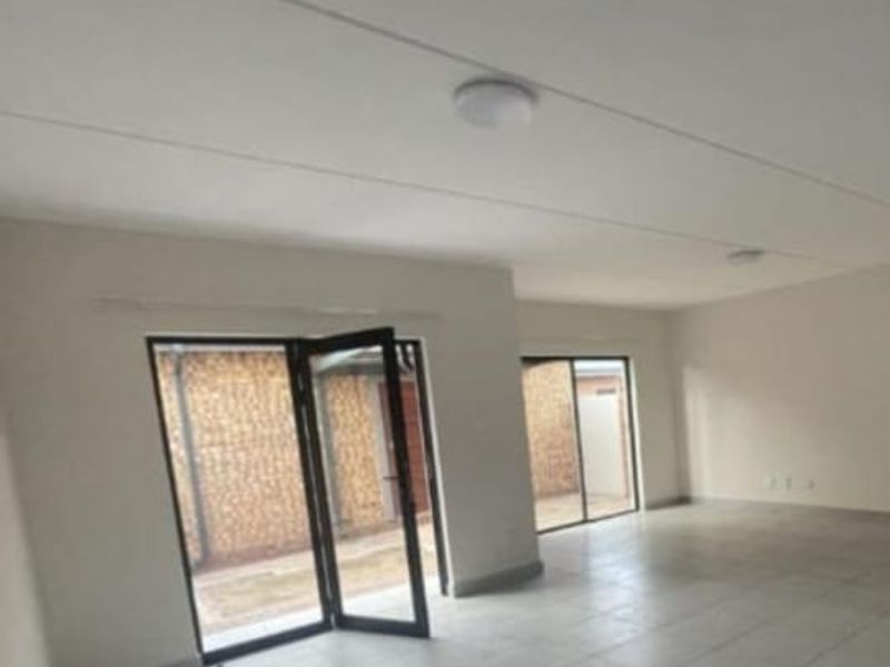 Spacious, empty living area featuring neutral tiled flooring and large aluminium framed glass doors providing access to the exterior.