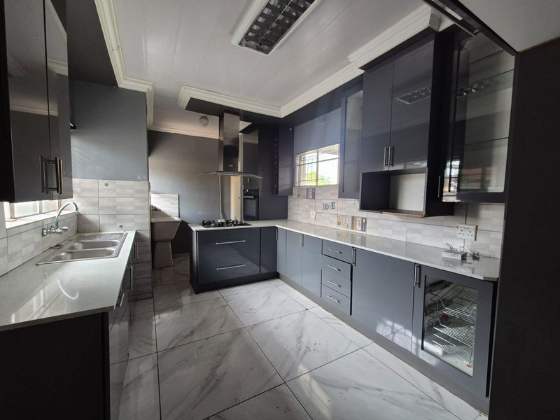 Modern kitchen featuring dark grey cabinetry, stone countertops, gas hob, extractor fan, and tiled flooring. The space is vacant and ready for final finishing touches.